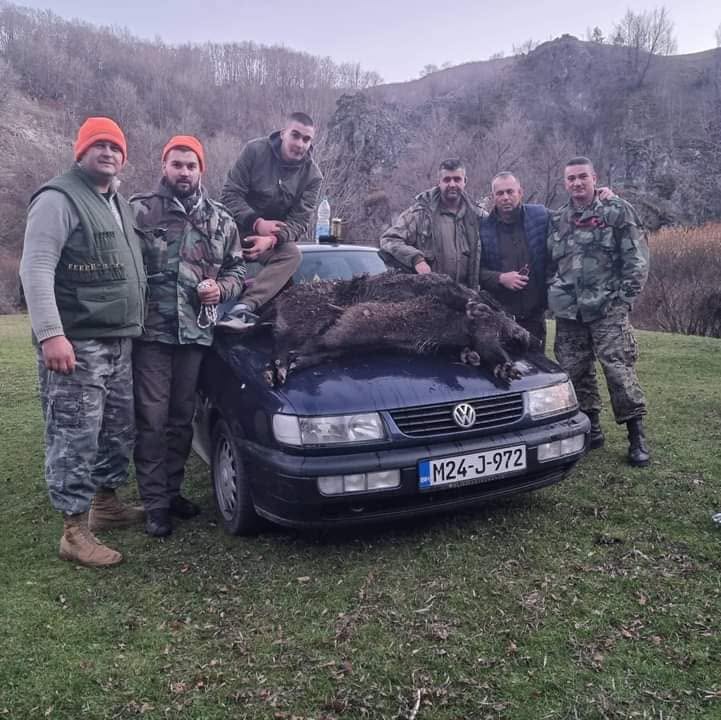 Šest lovaca u maskirnoj odjeći pored automobila na livadi, u podnožju stjenovitog brda